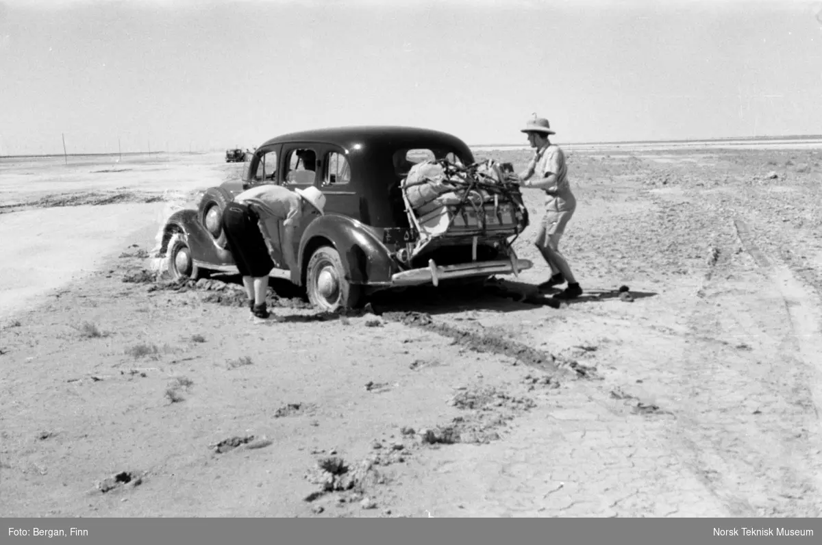 To personer jobber med å få løs bil som har kjørt seg fast i ørkensand