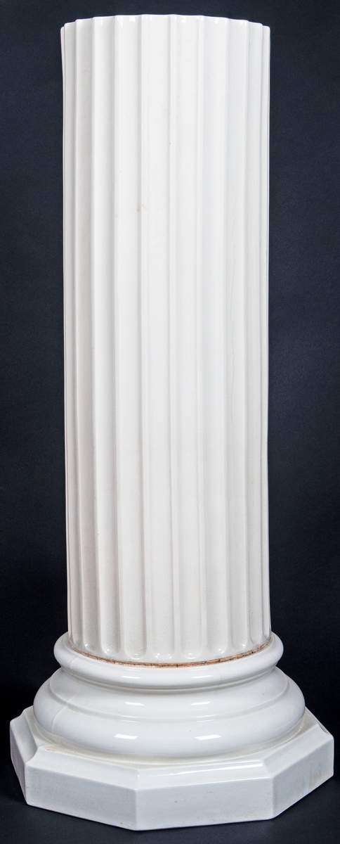 Piedestal, vitt porslin. Kannelerad kolonn med profilerad fot på åttakantig fotplatta.