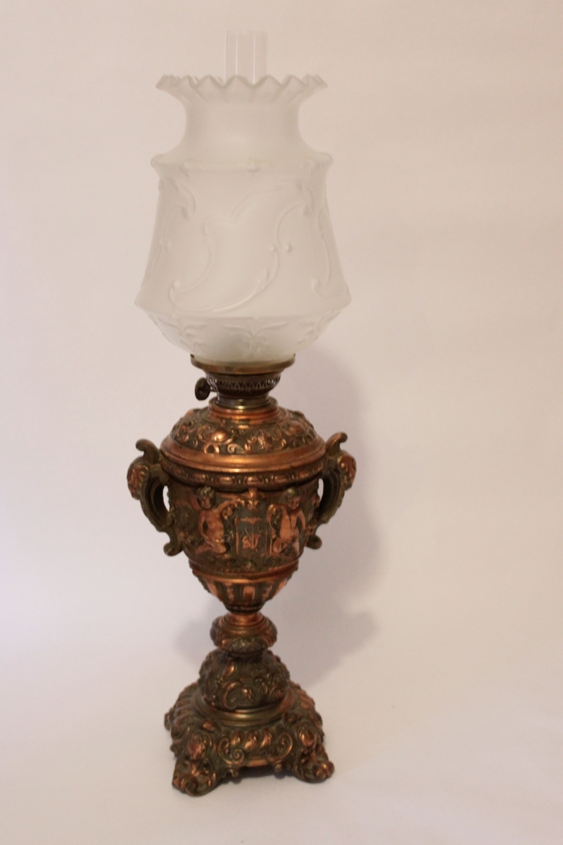 Lampfot från sent 1800-tal rikt dekorerad med bland annat en vapensköld flankerad av små putti. Lampskärm i frostat dekorerat glas.