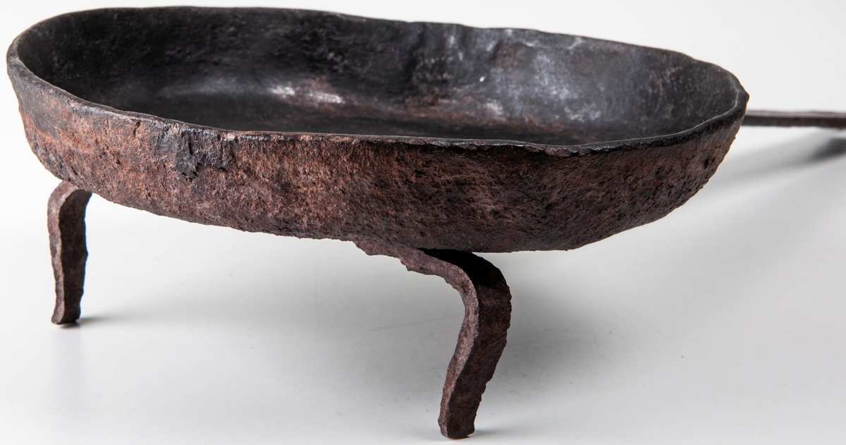 Stekpanna av järn, rund med uppåtstående kanter, Vridbart fästad på rakt skaft. Diameter 18 cm.
På tre ben, varav ett saknas.