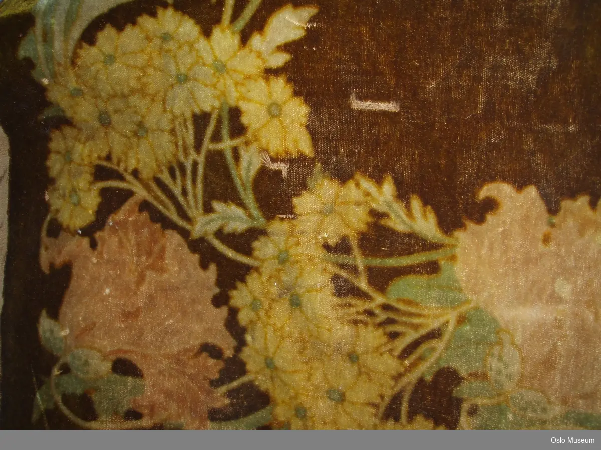 Gull- brun fløyelsduk fra slutten av 1800- tallet (ant.)
Duken er kvadratisk med blomstermotiv langs kantene, i lyse duse farger i grønn, gul og rosa. Baksiden er trukket med et grovt brunt stoff.