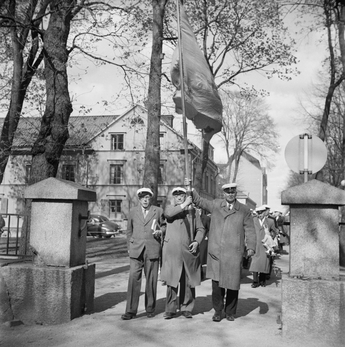 Män i studentmössor vid grindarna till Uppsala gamla kyrkogård, Östgöta nations minneslandskap, Uppsala 1949