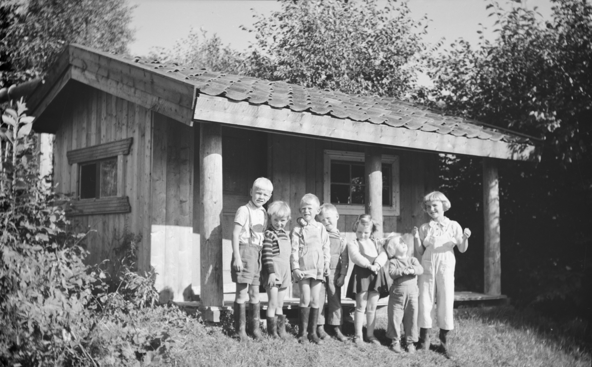 Sju barn foran en liten hytte