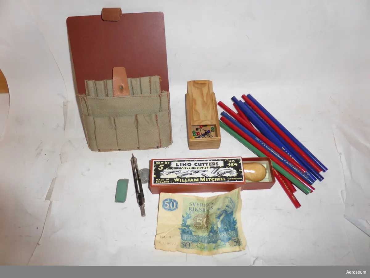 En brun postväska gjord i läder, canvas, och hård pappkartong. Innehåller en 11 stycken pennor som aldrig vässats, en enkrona från 1978, en gammal 50-kronorssedel tryckt 1980, en liten passare, ett använt suddgummi, en kartong med linoliumskärare, och en trälåda med knappnålar i olika färger.