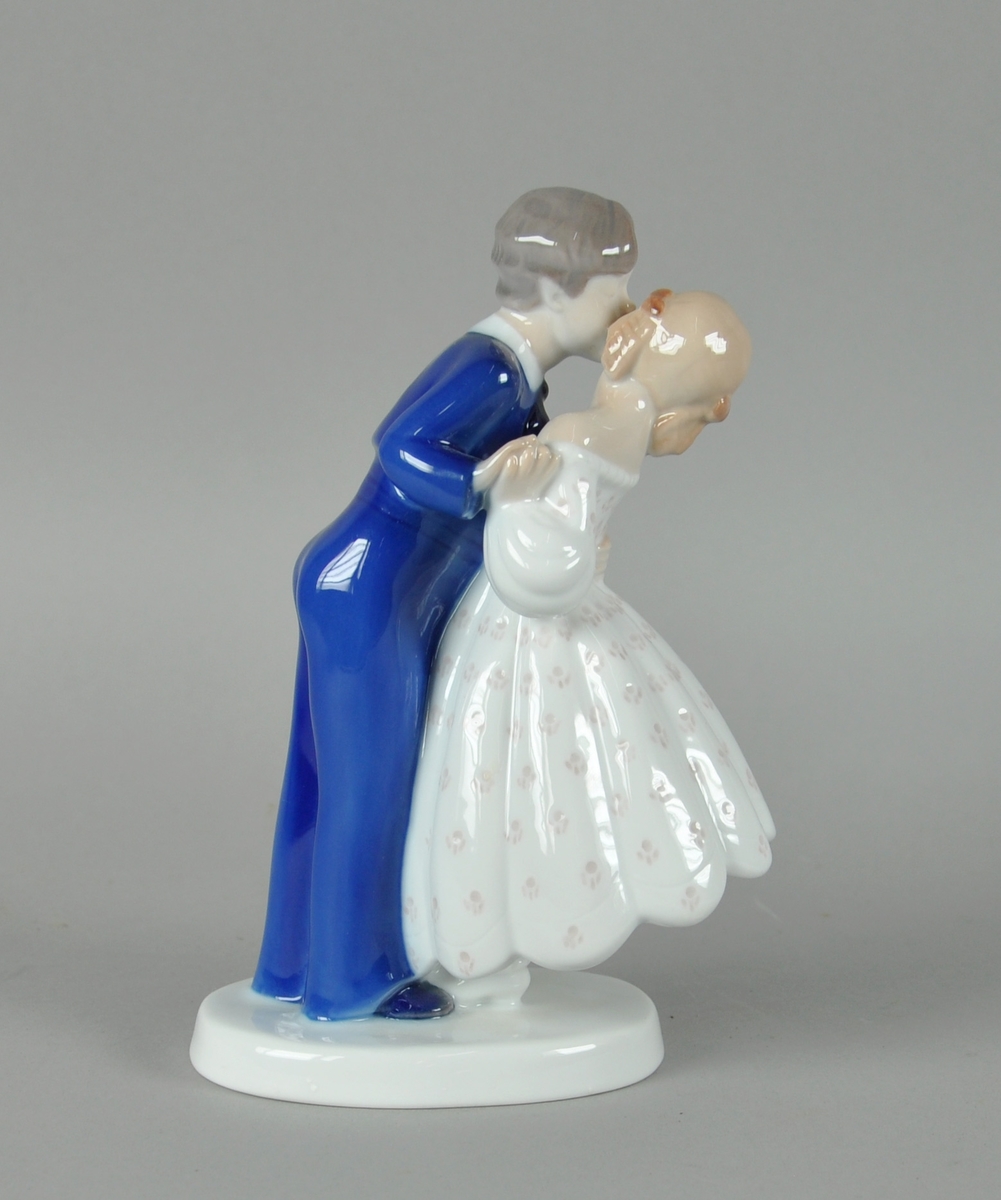 Skulptur av glassert keramikk, med fargedekor. Skulpturen forestiller gutt som kysser jente på kinnet. Skulpturen står på en oval sokkel.