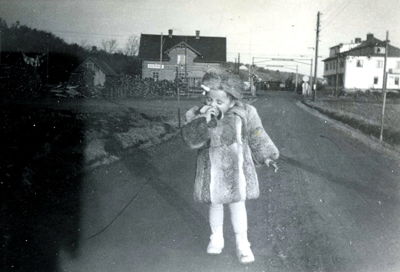 Gullevi Persson Andersson (född 1945) äter banan ståendes på Labackavägen år 1950. Hennes morbror Nils Eriksson, som var körsnär, hade sytt pälskappan. Till vänster ses Kållereds station och till höger Svenssons Lanthandel Gustavsro där Gullevi bodde med sina föräldrar.