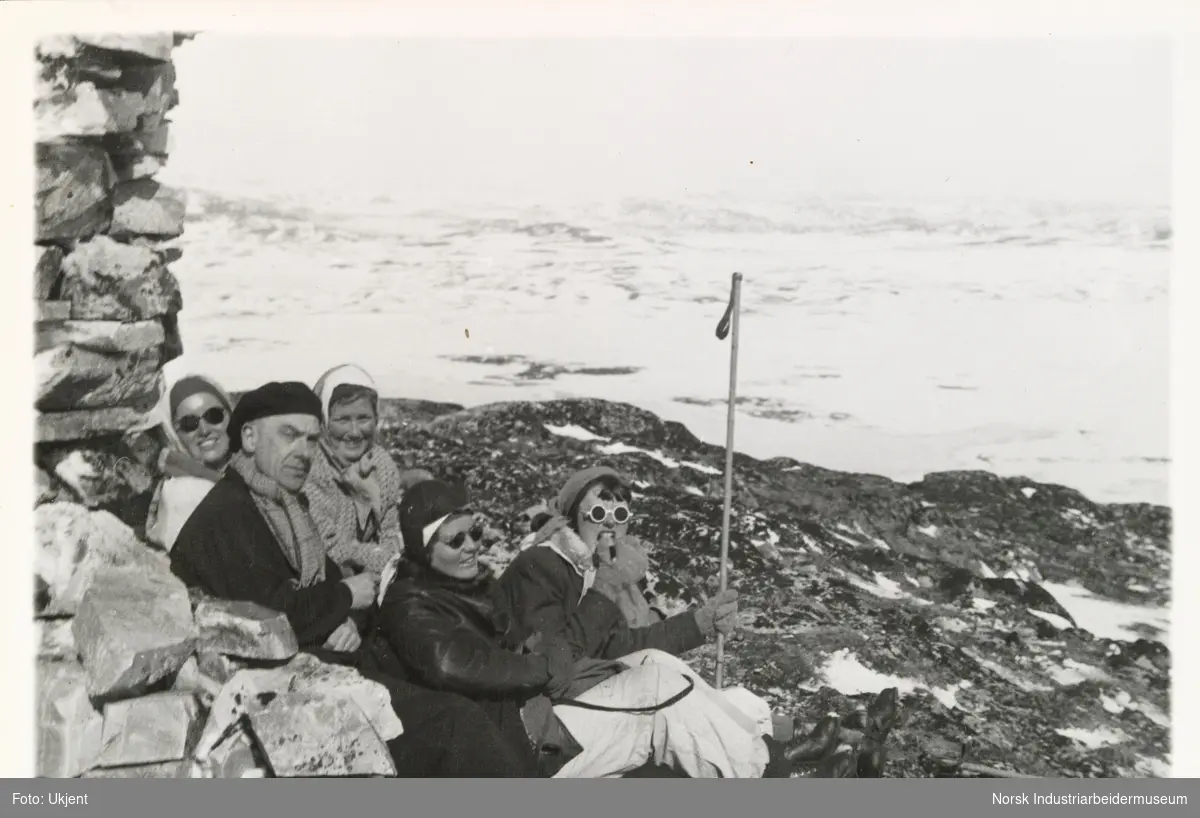 En mann og fire kvinner sitter ved varde i turantrekk på fjellet