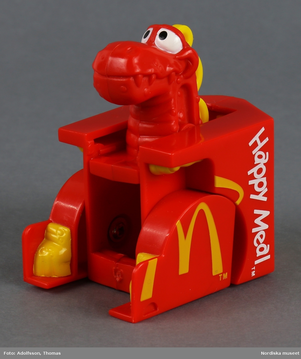 Leksak i form av en röd matkartong för hamburgare. På utsidan finns texten "Happy Meal" och symbolen M som står för matkedjan McDonald's. Sidorna går att fälla ut, varvid en djurfigur med huvud och tassar framträder.