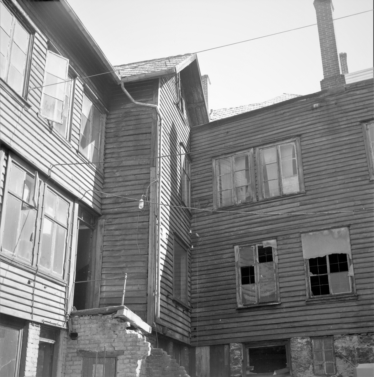Bybebyggelse. Riving av en bygning i Haugesund sentrum. Bygninger på begge sider. Utsikt til sundet. Gravemaskin i arbeid. Brolagt gate. Bestilt av Skipsreder Amlie