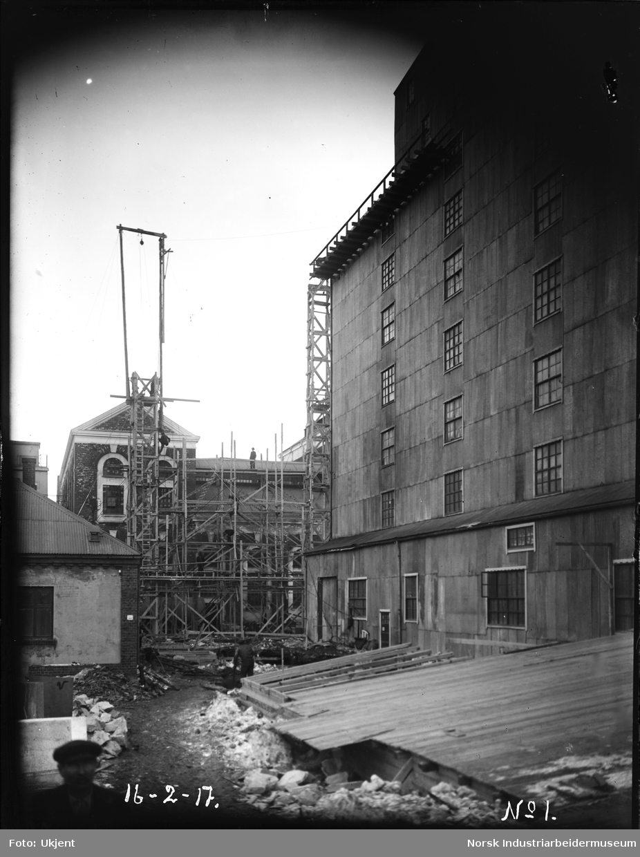 Arbeid inne på fabrikkområdet til Norsk Hydro. Reisverk løftes med kran til bygg for syretårn.