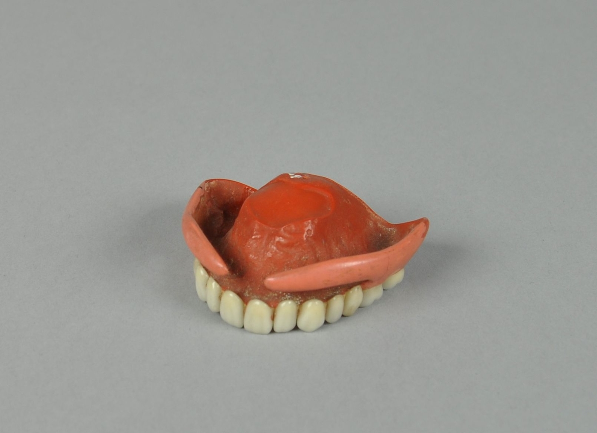 Tannprotese av plast, består av en støpt plate med 14 tenner av porselen