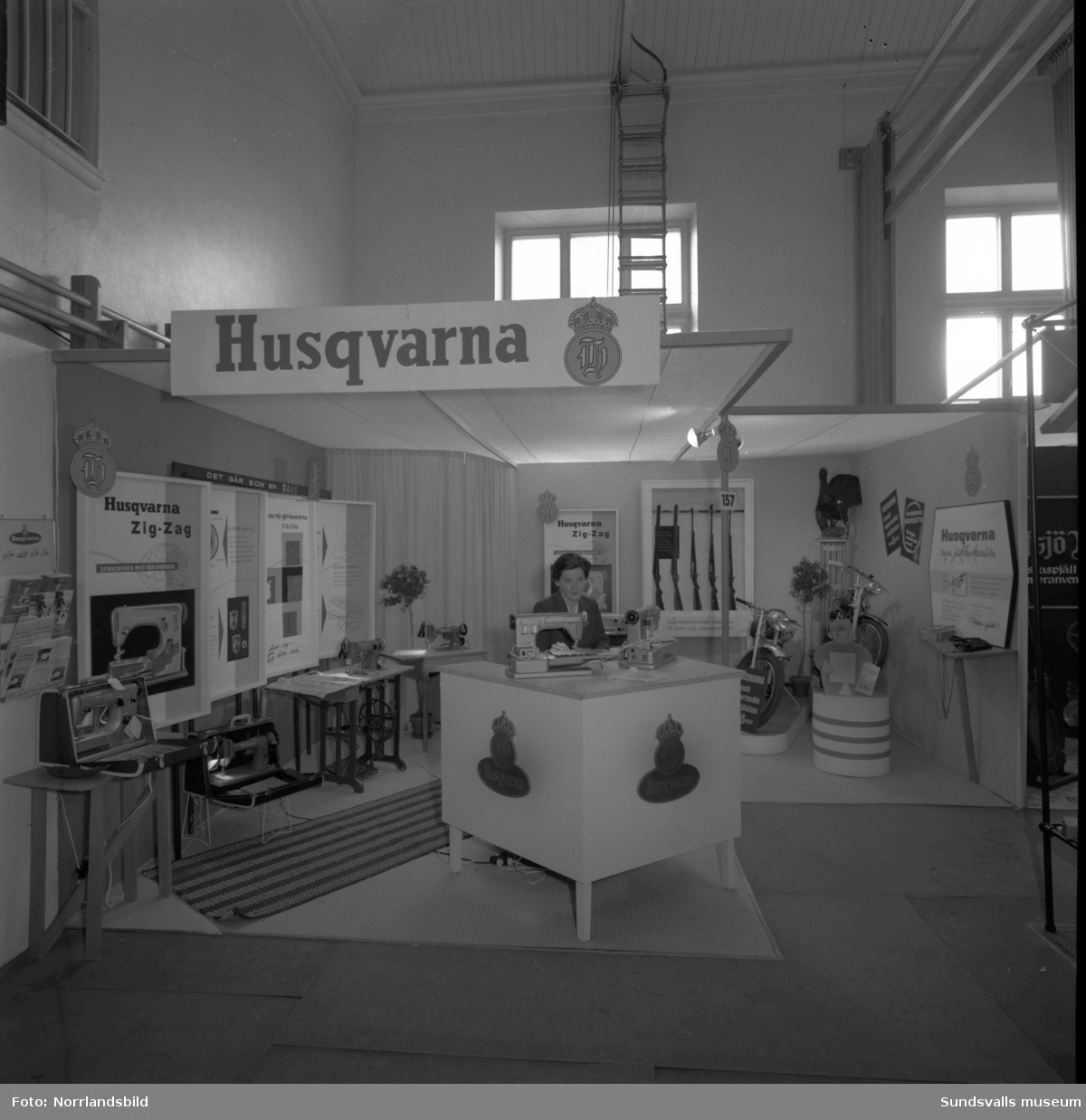 Husqvarnas monter i Läroverkets gymnastiksal på Sundsvallsmässan 1955.  Bland annat visas mopeder, vapen och symaskiner.