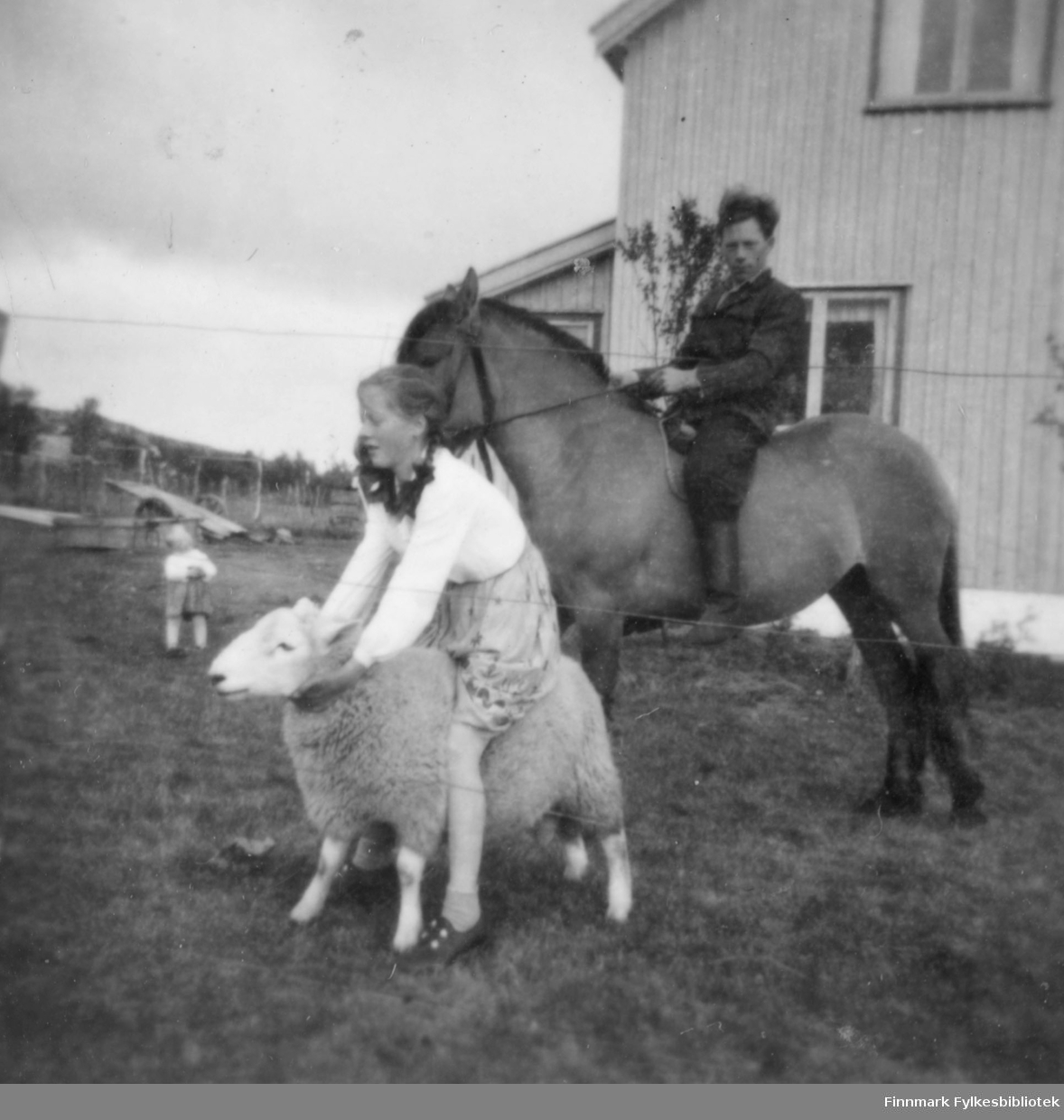 Anna Agnethe Mathisen rir på en sau og farbroren Nils Mathisen rir på en hest. Et ukjent barn står litt i bakgrunnen.