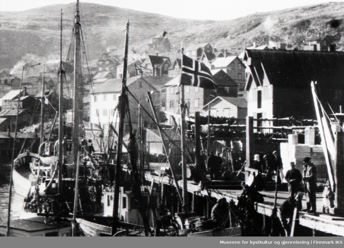 Honningsvåg havn. Flere båter ved kaia ved en av fiskebrukene. I bakgrunnen deler av bebyggelsen. 1930-årene.