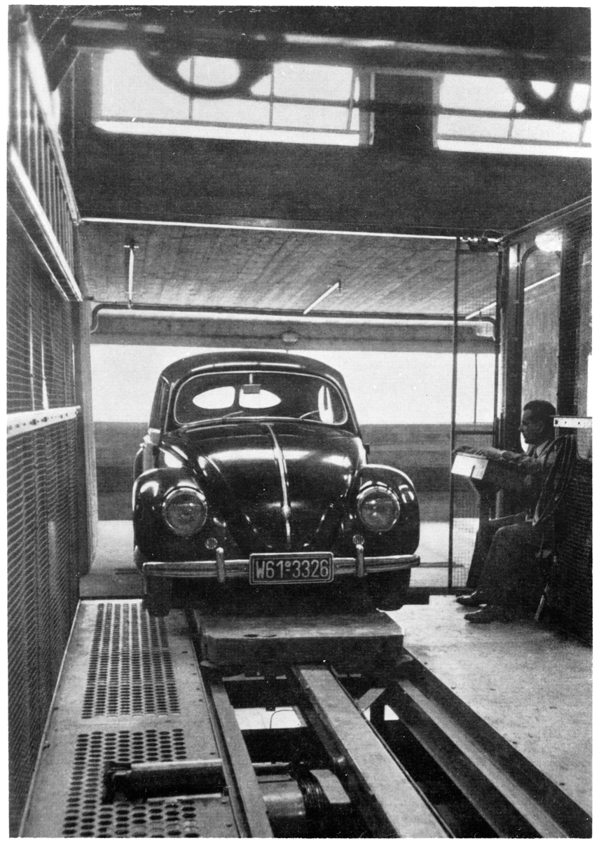 Personbil stående på hissanordning inne i parkeringshus i Karlsruhe, Tyskland. Till höger sitter en man som reglerar hissen.