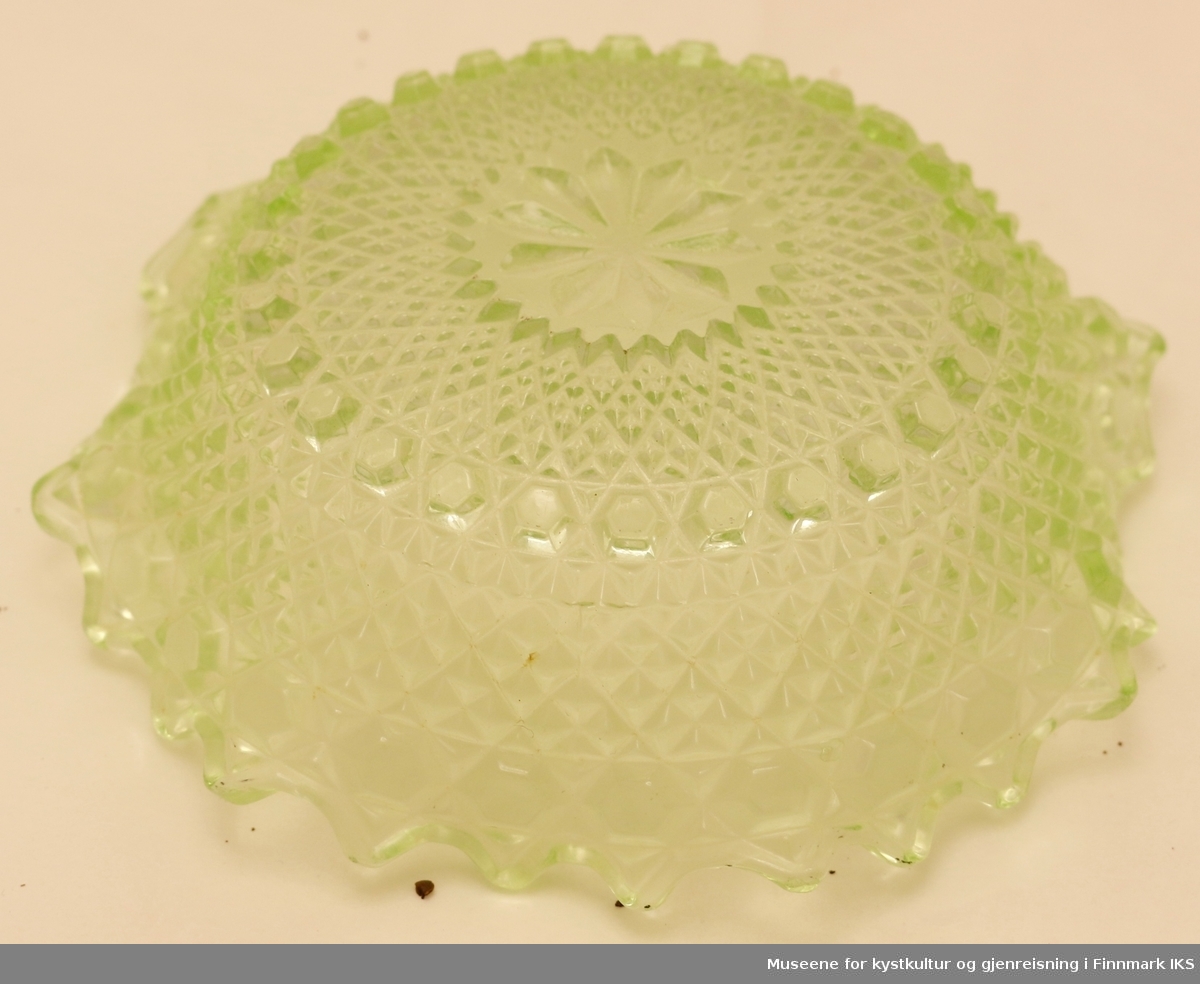 En grønn glasskål med presset mønster på utsiden og buede kanter