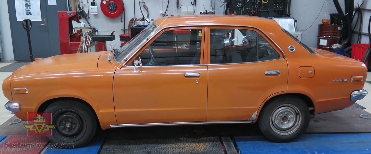 Mazda 818 Deluxe. 4-dørs sedan karosseri, oransje (Herschel Orange) lakk utvendig. Svart interiør med hvitt taktrekk. Bilen har en SOHC, vannavkjølt, bensindrevet 4-sylindret rekkemotor med et sylindervolum på 1272 kubikkcentimeter. Enkel forgasser. Motorytelse/effekt 69 hk. To aksler, bakhjulstrekk. 4- trinns manuell girkasse med girstang i gulvet. Antall sitteplasser er 5. Km. stand på telleren er 7384 km (i virkeligheten rullet 107 384 km). Standard dekkdimensjon foran og bak er 155 SR 13. Felgene er 4.5 " brede.