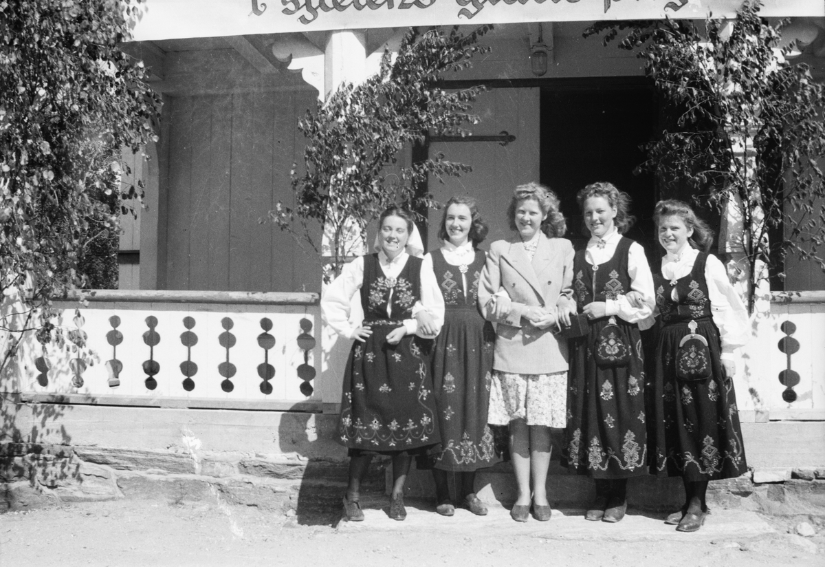 Gruppeportrett av fem unge damer foran et hus, tilsynelatende pyntet til 17. Mai.