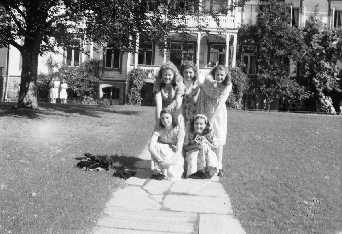 Gruppeportrett av fem jenter foran et større hus.