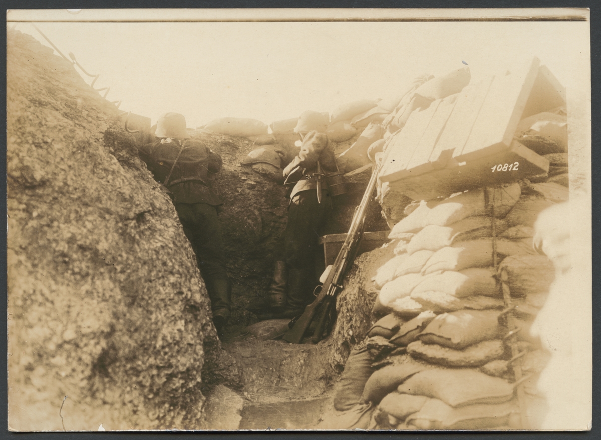 Bilden visar två soldater som tar skydd bakom sandsäckar i en skyttegrav.