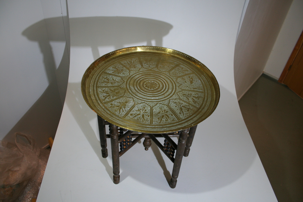Bordet består av et brunt, sammenleggbart understell med dreide kuler, messingbrett med gravert dekor. Brettet ligger løst oppe på understellet. Røkebodet er i orientalsk stil.