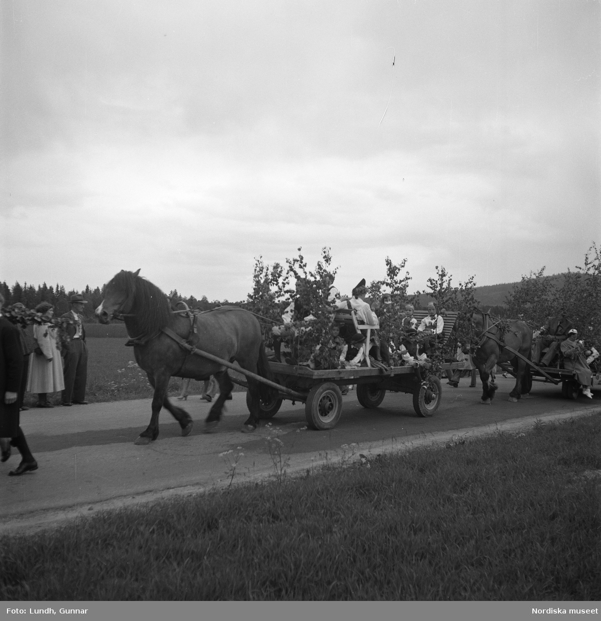 Motiv: (ingen anteckning) ;
Porträtt av en kvinna i folkdräkt och en man som sitter på marken, män och kvinnor i folkdräkt går i ett proccesionståg med flaggor och kvinnor bär en lövad girlang, människor åker på en hästdragen vagn, en folksamling går i ett processionståg.
