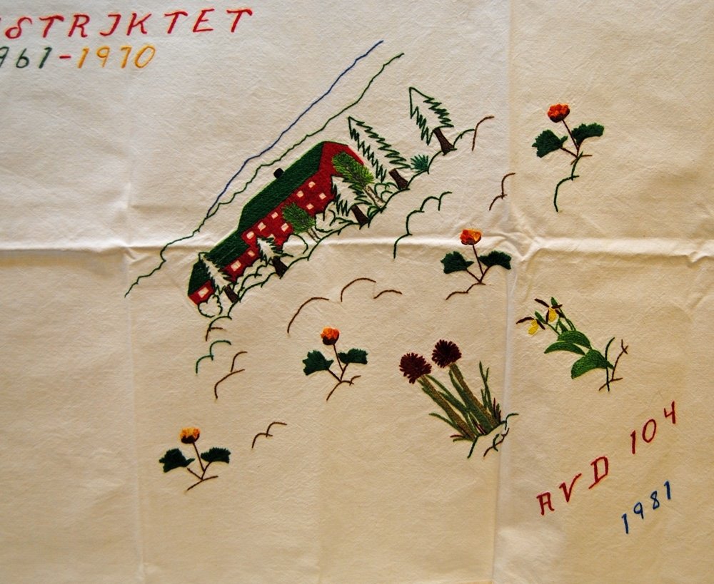 Duk, broderad av det s.k. Kvinnorådet inom JHF (Järnvägsmännens Helnykterhetsförbund), i stjälksöm och dubbelsidig plattsöm med färgat garn på vitt bomullstyg.

Motiv med symboler från fyra olika avdelningar. I mitten står "IX DISTRIKTET 1961-1970".
Hörn 1: "AVD 59 SUNDSVALL", medelpads landskapsvapen (blå, vit, röd, vit, blå rand), en skvader (ett fantasidjur vars framdel är en hare och bakdel en tjäder, djuret är en inofficiell symbol för Sundsvall) samt en byggnad från friluftsmuseet på norra berget och utkikstornet "Glasspinnen" på samma plats. 
Hörn 2: "AVD 105 HÄRNÖSAND", ångermanlands landskapsvapen (tre fiskar samt krona på toppen av skölden), styvmorsvioler (landskapsblomma).
Hörn 3: "AVD 104", "1981", motiv av föreningslokalen Storvallen i Storlien utanför Östersund, brunkulla (landskapsblomma), guckusko (vanligt förekommande orkidé i Jämtland) samt hjortron.
Hörn 4: "AVD 58 ÅNGE", "MUNKBYSJÖN - SVERIGES MITTPUNKT", grankottar (Medelpads landskapsblomma) samt en kaducé med bevingat hjul (SJ:s symbol).