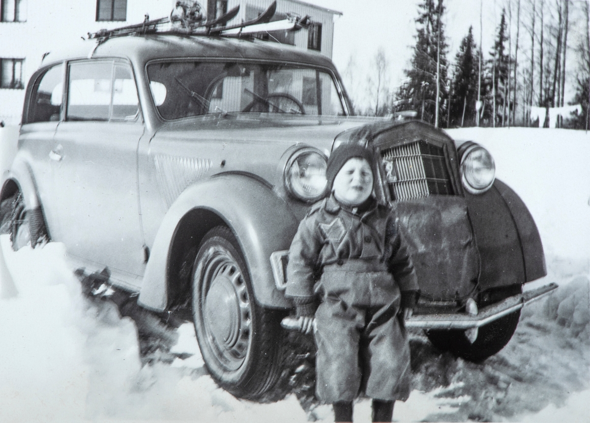 Erik Nordstad sittende på støtfangeren til en bil, på Harildstad Øvre, 333/1. Vinter, snø. Bil. Opel Olympia eller Kadett 1937-38.
