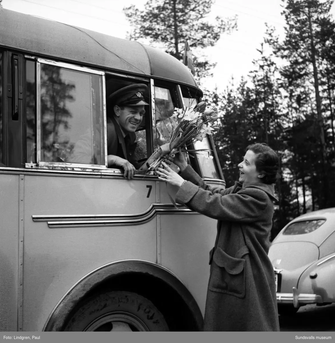 Invigning av ny busslinje, Sandarna-Sundsvall. Bussen går för första gången genom Solbacka, vilket var efterlängtat av de boende i byn. Busschauffören uppvaktas med en blombukett av en glad Solbackadam.