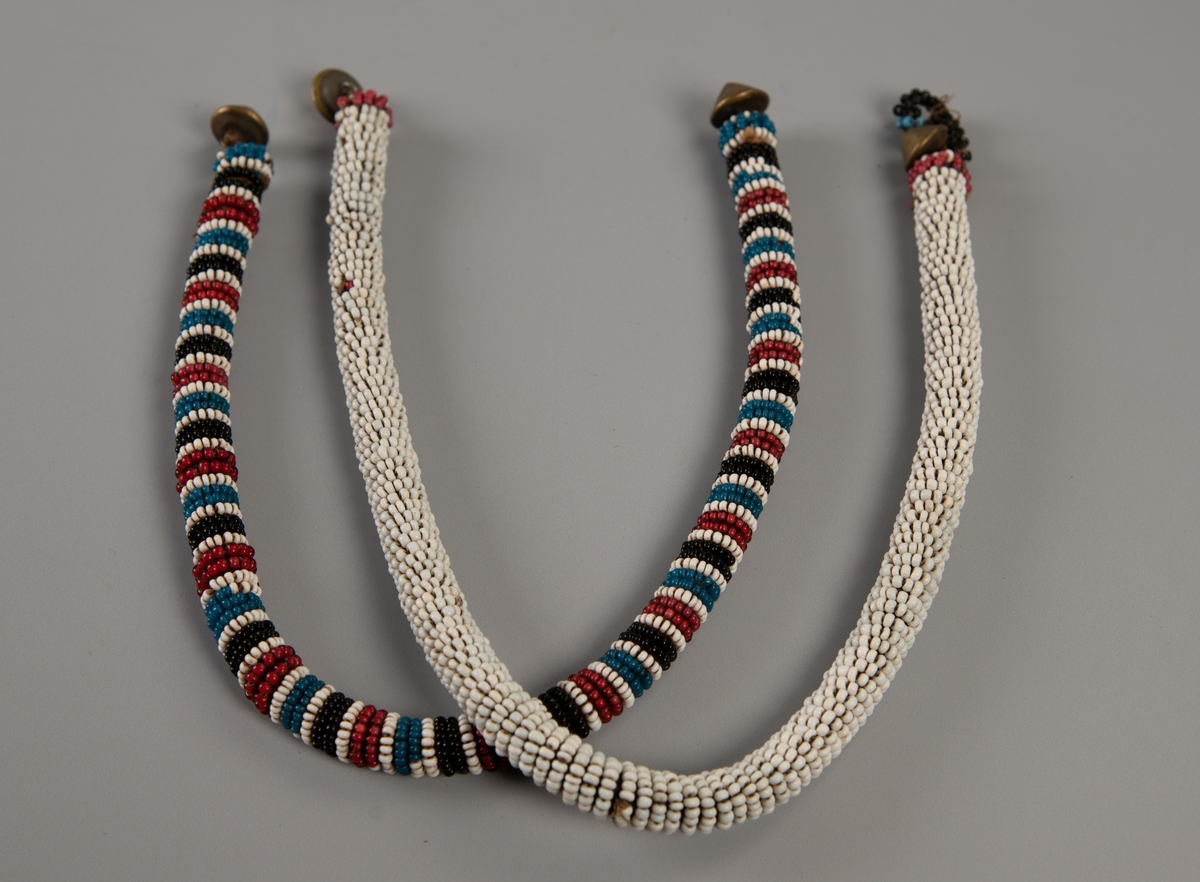 Litt tykk perlesnor med tverrader i sort, hvitt, egyptisk blått og rødt. I hver ende en spiss messingknapp. Hempe mangler.