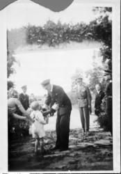 Bilde av Kong Haakon i uniform som hilser på et barn med mil