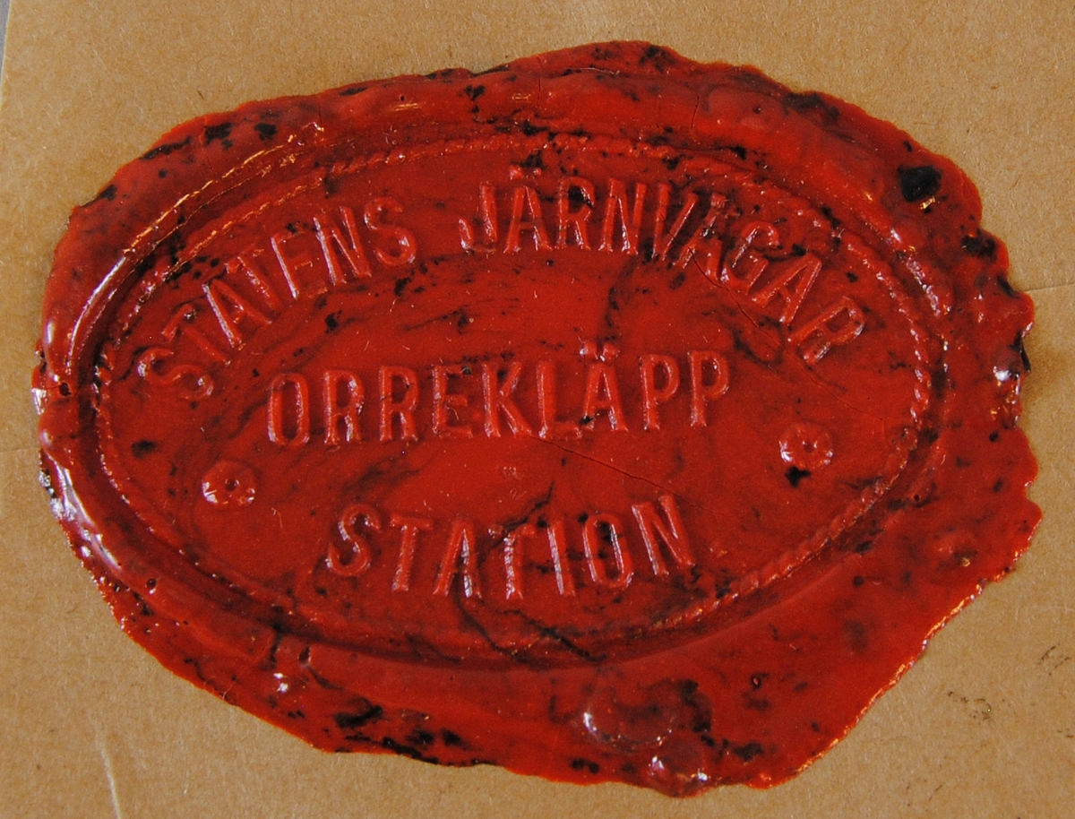 Sigillavtryck av rött lack på brunt papper. Avtrycket är format som en liggande oval.