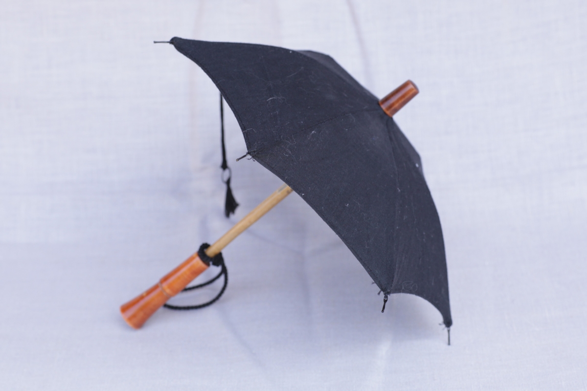 Leke- eller dukkeparaply med svart skjerm og metallspiler. Håndtak i lakkert tre.