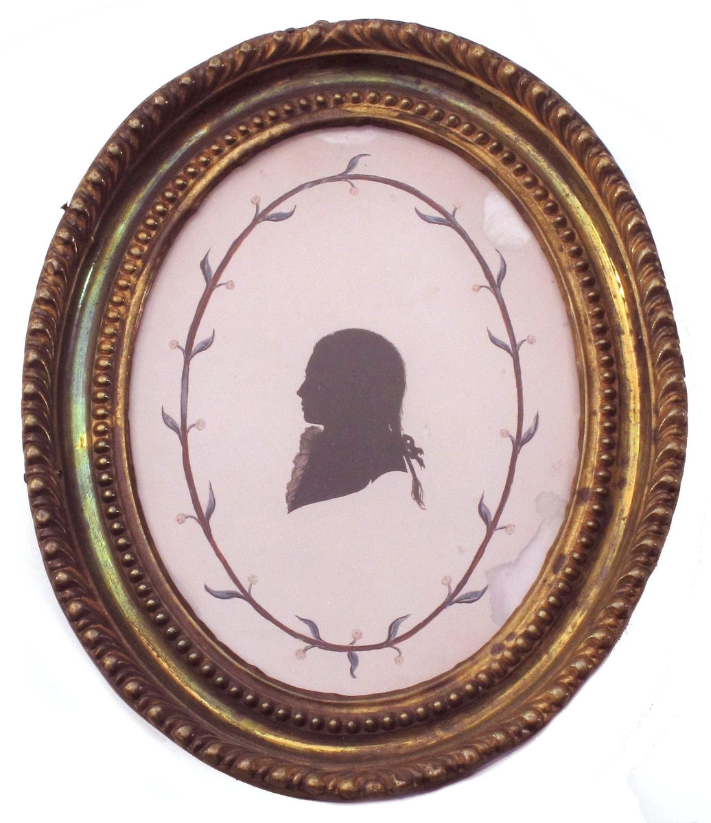 Liten silhouett  av v. vendt ung mann med hårpisk med sløyfe og kalvekryss, avskåret ved skuldrene.  Omgitt av en brun oval ring med blå blad og små gule blomster.