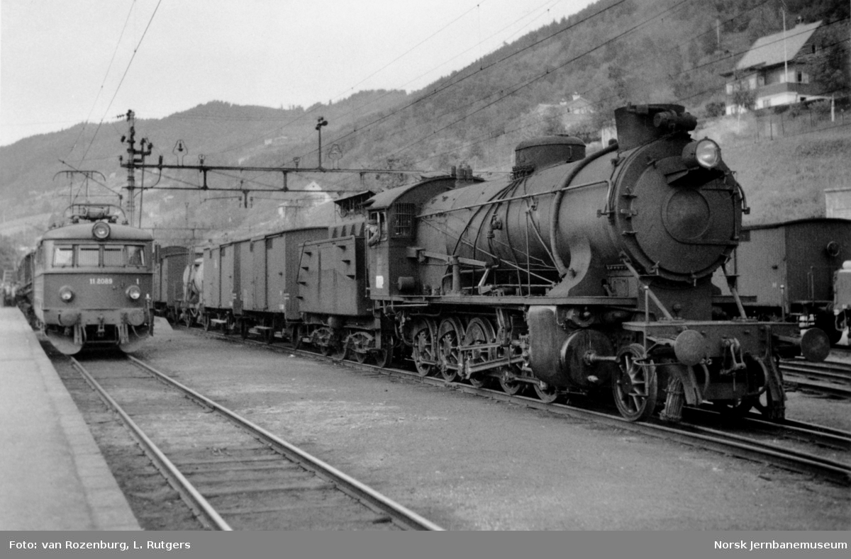 Damplokomotiv type 39a nr. 166 med godstog retning Oslo på Voss stasjon. Bak til venstre elektrisk lokomotiv El 11 2089 med persontog