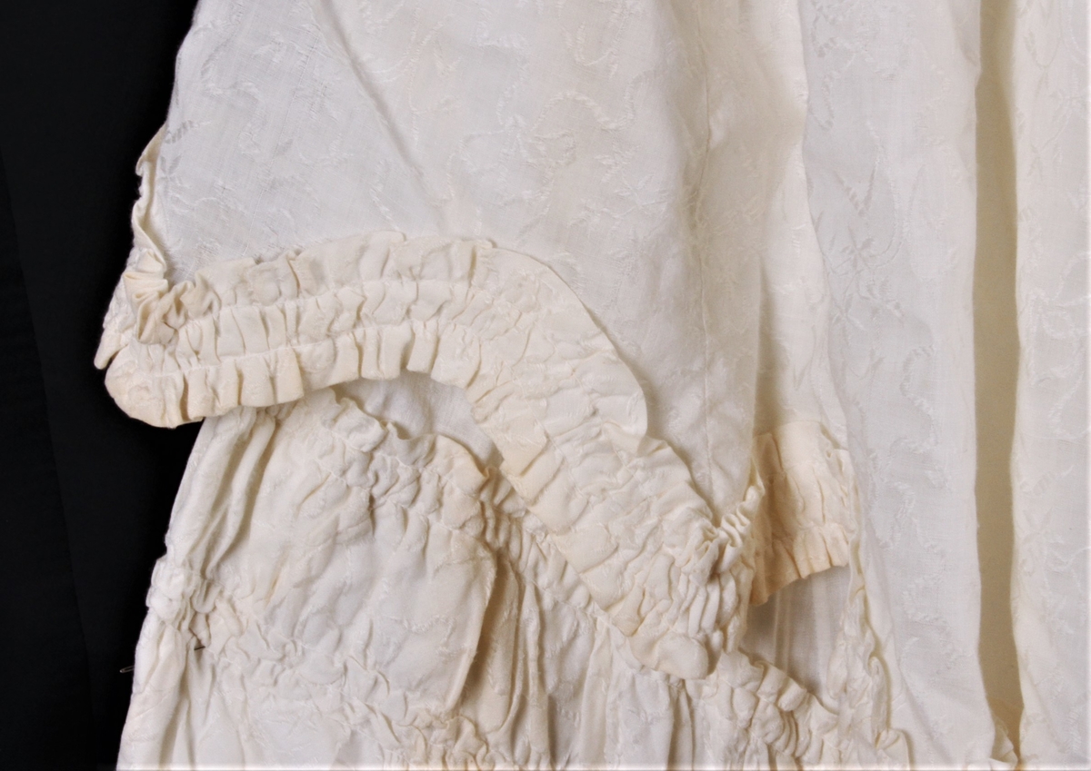 Kjolen er av ullmusselin som har innvevet mønster av silkeblomster, den har foran en liten rynke fra kragen og 12 cm nedover, den er knappet i ryggen med 13 possementknapper, den har en liten krage knappet med to trykknapper, lange puffermer og trange underarmer, her er to spiler i ryggen og enliten åpning i venstre side, lukket med trykknapper, overkjolen har rubbing i tunger, skjørtet har rubbing som går helt rundt, slepet er festet til underkjolen og har også rubbing i kanten, underkjolen har knapper i kantendisse har små tunger som ble hugget ut med et spesialjern, hele kjolen ble sydd av Amalie Faarlund og hun brukte den i sitt bryllup i 1905 da hun ble gift med lærer og løytnant Knut Fugllien. Datteren Aud brukte kjolen i sitt bryllup.