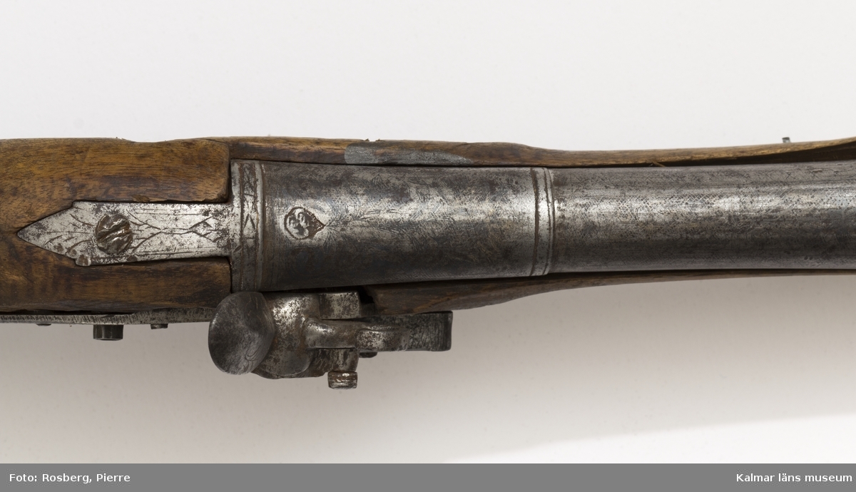 KLM 14261 Pistol, med flintlås. Orientalisk pipa, vidgad i mynningen. Helt silverinkrusterad. Lås och kolv senare. Hanen saknas. Så kallad trombon. Datering, 1700-talets senare hälft.