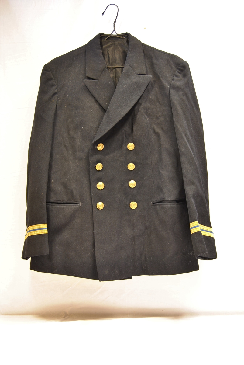 Sort uniformsjakke, 8 messingknapper med anker i front og to gullstriper på blå bakgrunn på ermene. Rette lommer i sidene og innerlomme på jakkens venstre side.