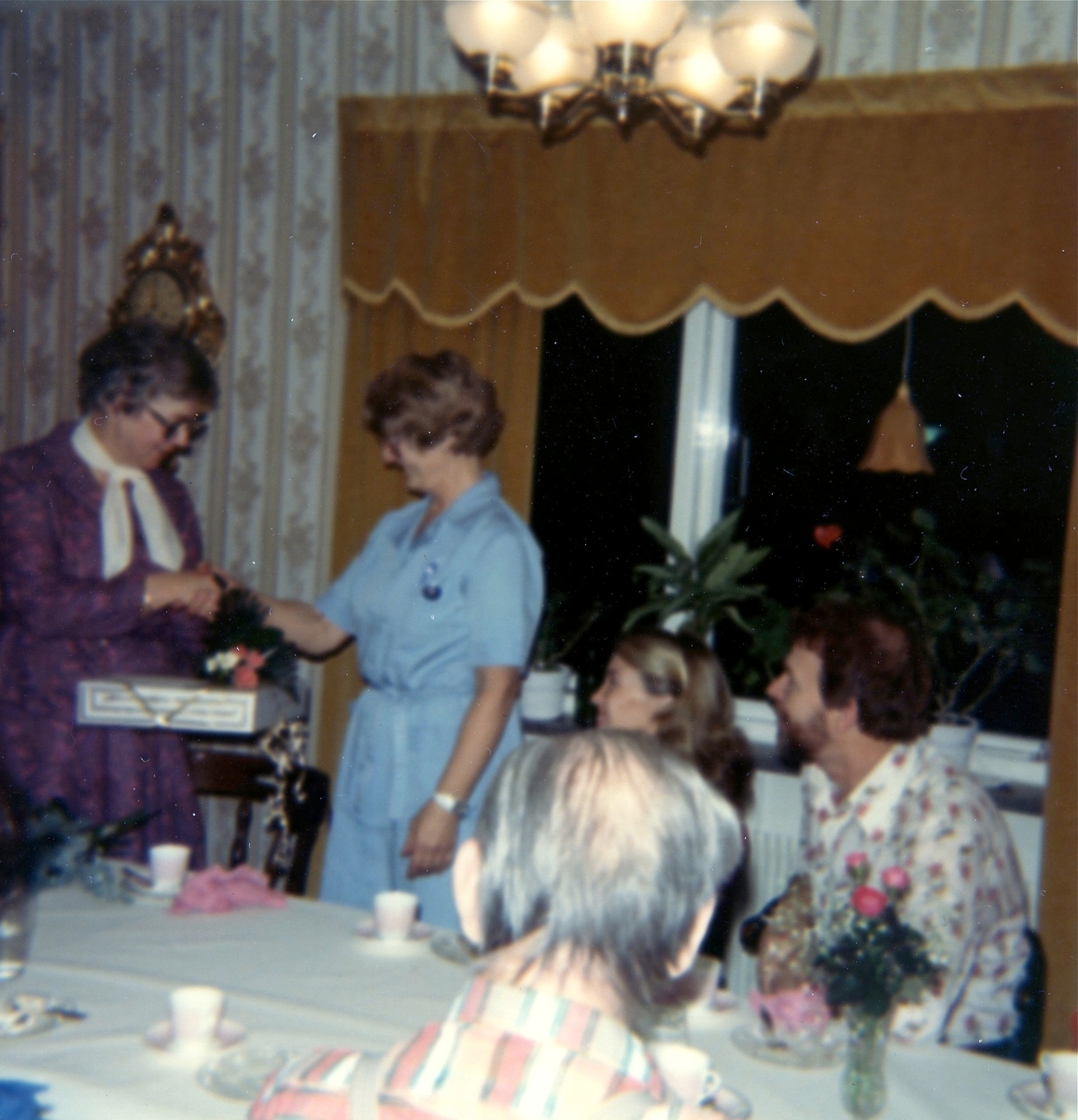 Avtackning av Inga Svanberg som ska gå i pension, år 1982. Hon hade arbetat som kokerska på Brattåshemmet (gamla ålderdomshemmet). Från vänster: Inga Svanberg, Aina Ekstedt (föreståndare), Inga Britt (vårdbiträde) samt Ralf (vaktmästare). Okänd man i förgrunden.