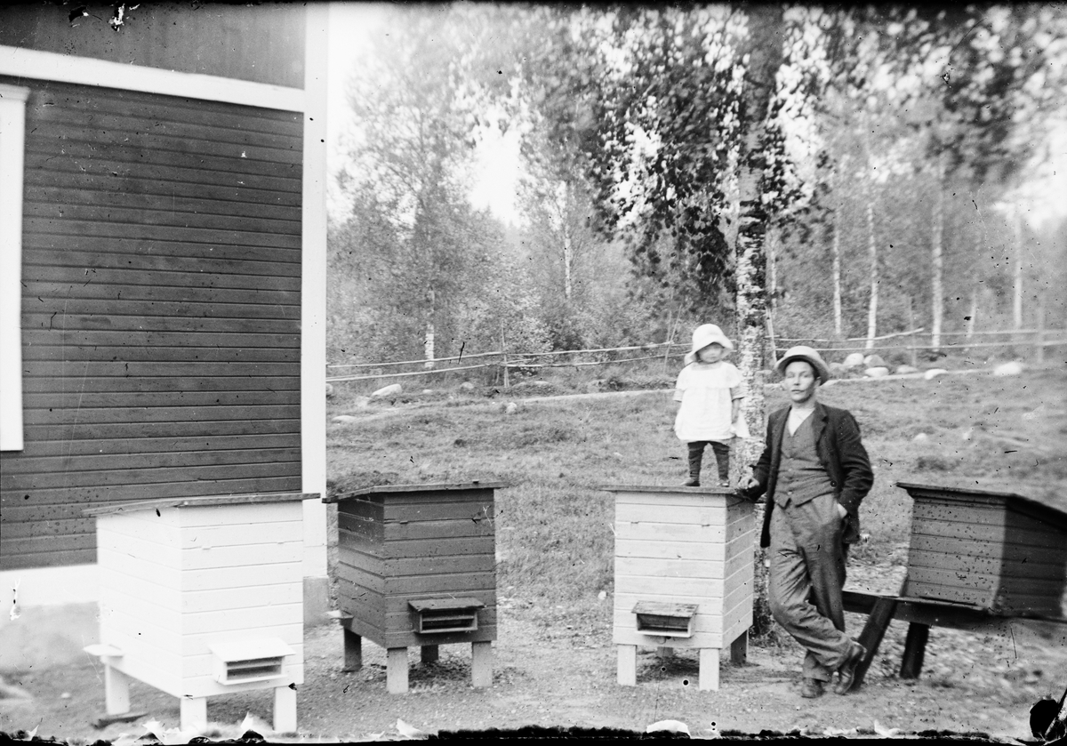 Ett barn står på en bikupa, en man står bredvid, Östhammar, Uppland