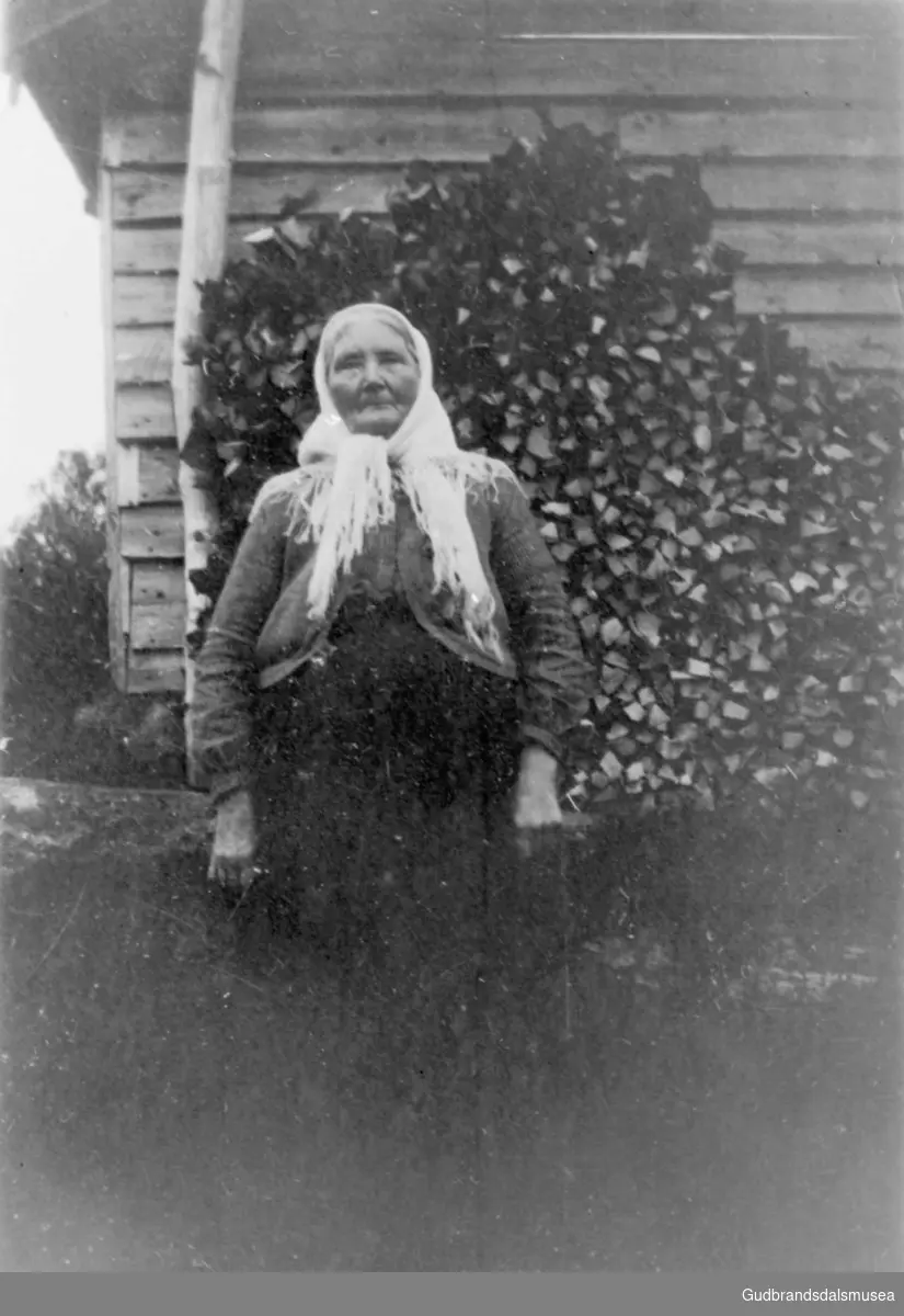 Portrettbilde, eldre kvinne ute i hagen, på hushjørnet. Dette er kanskje siste gangen Marit var i Holen.
