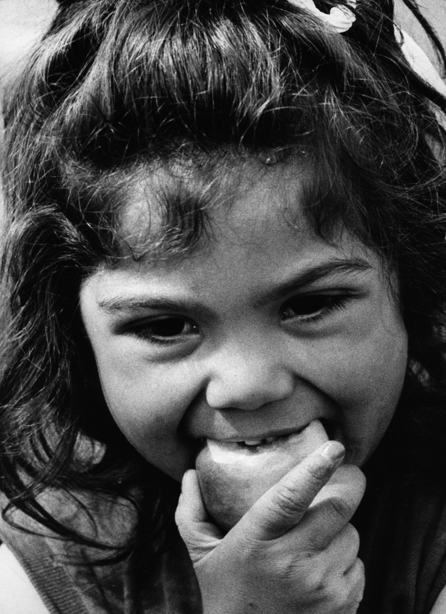 En romsk flicka äter ett äpple. I håret har flickan en rosett.