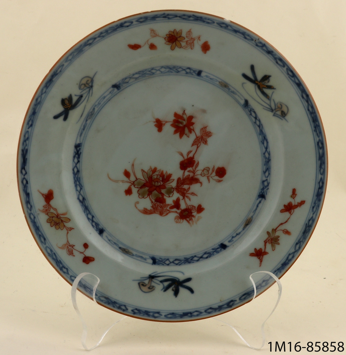 Tallrik av blåvitt kinesiskt porslin, flat och med slät kant. Dekorerad med blommotiv och bårder i blått, rött och guld