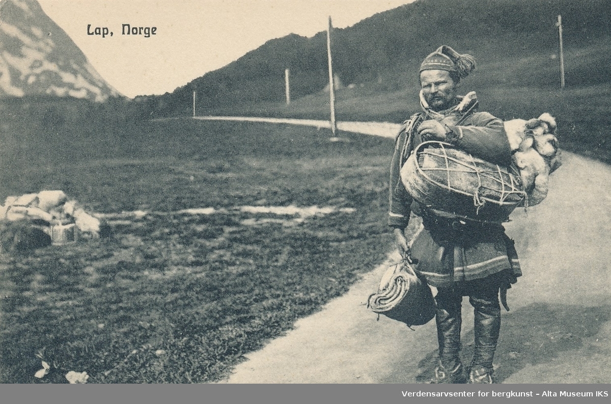 En samisk mann på en veg. Han er ikledd kofte og lue mens han bærer på en ryggsekk og annen bagasje.