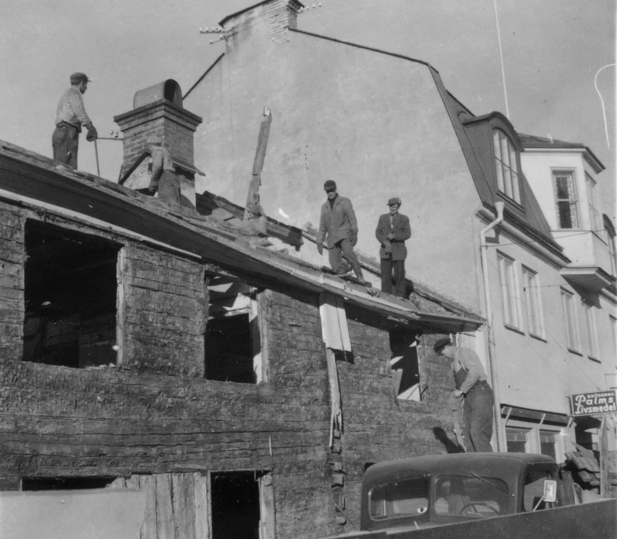 Rivning av 1700-talsfastighet på Brahegatan 51. Fastighetens panel är borttagen liksom fönsterbågar. Fyra män står på taket.