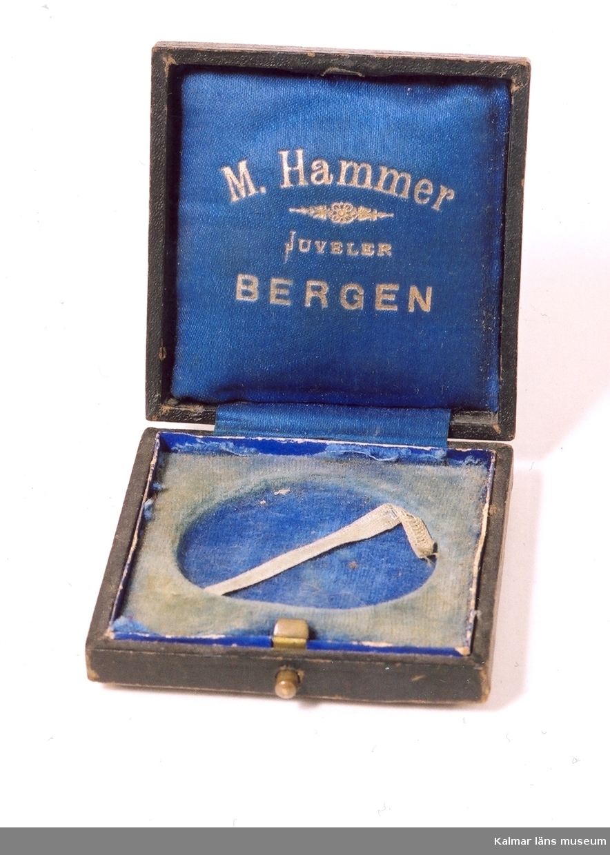KLM 39586:54 Medalj av metall och tillhörande ask av trä, papp och textil. Medaljen är monterad på diplomets ram (KLM 39586:60). Bronsmedaljen tilldelades Gustaf Axteliu, vid Udstillingen Bergen, Norge 1898.