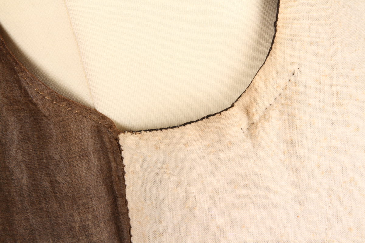 Enkeltkneppet silkevest i svart silkebrokade. Silkebrokaden har innvevde sølvtråder som danner mønsteret. Rygge er i brunt linstoff, og har snøring midt bak. Vesten er foret med hvitt linstoff. Hele vesten er sydd for hånd, i hovedsak med lintråd. 