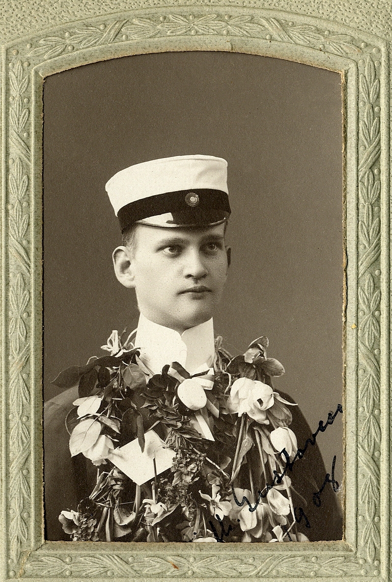 En man i bonjour med stärkkrage, studentmössa och med en massa blombuketter. I nedre högra hörnet syns inpräglat årtal: "1909". Där syns också en autograf: "Wilh. Gustavsson, 1908". 
Bröstbild, halvprofil. Ateljéfoto.