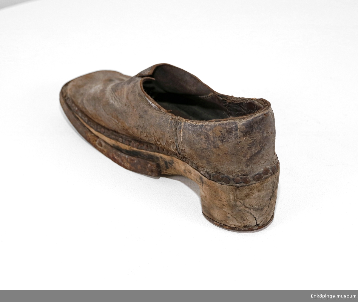 Sko med träbotten och överdel av skinn. Skon är förstärkt med metall runt klacken och sulan. Skon är från 1700-talet.