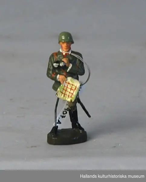 Leksakssoldat av trämassa på ståltrådsskelett i tysk uniform. Målad i grönt, brunt, svart, rött och skärt.